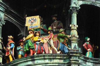An Array Of Colorful, Historic Figures Displayed Behind A Protective Mesh In Munich, Possibly A Detail From An Ornate, Mechanical Clock Tower, Where Intricately Dressed Sculptures Prepare To Enact A Traditional Hourly Show.