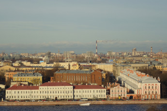 A Panoramic View Of St. Petersburg With Neoclassical Architecture, Smokestacks In The Distance Emitting Smoke, And A Clear Blue Sky, Showcasing Urban Life And Industrial Activity.