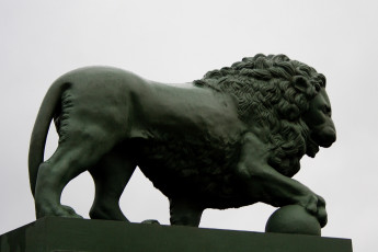 A Majestic Bronze Lion Statue, Presented In Profile, Stands With A Poised And Muscular Posture Atop A Stone Plinth Against A Gray Sky In St. Petersburg.