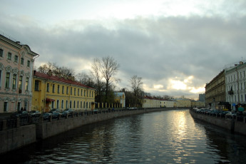 A Serene Dusk Over A Calm Canal In St. Petersburg, Flanked By European Classical Architecture Under A Cloud-Streaked Sky, Reflecting The Waning Light.