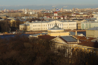 An Aerial View Of A Historic Neoclassical Building In St. Petersburg Basking In The Golden Hues Of The Setting Sun, With A Sprawling Cityscape And Cloudy Skies In The Backdrop.