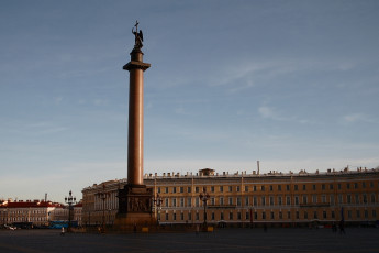 The Alexander Column Towers Over Palace Square In St. Petersburg At Dusk, With A Bronze Angel Holding A Cross At Its Peak And The General Staff Building Stretching In The Background Under A Clear Sky.