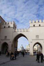 An Archway In Munich Leads Into A Bustling Square Where Pedestrians Walk Under A Clear Blue Sky.