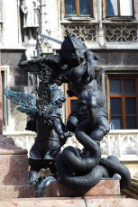 A Bronze Statue Depicting A Winged Warrior Engaged In A Fierce Battle Against A Serpentine Monster, All Set Against The Backdrop Of An Ornate Building With Classical Architectural Features In Munich.