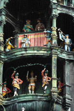 Clock Tower In Munich Featuring Finely Crafted, Colorful Mechanical Figurines, Possibly Depicting Historical Or Folkloric Scenes, Encased Behind Protective Netting, Showcasing Traditional Attire And Poised Mid-Motion To Simulate A Performance