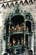 An Ornate Clock Tower In Munich With A Mechanical Performance, Featuring Vividly Colored Figures Akin To Royalty And Jesters, Set Against A Gothic-Style Architectural Backdrop.