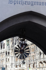 An Antique Bicycle Hangs Beneath An Arched Stone Entryway Emblazoned With &Quot;Spielzeugmuseum,&Quot; With The Ornate Facade Of The New Town Hall In Munich, Germany, Visible In The