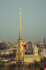Golden Spire Of The Peter And Paul Cathedral, With The Russian Flag Fluttering Below, Rises Above The Historic Skyline Of St. Petersburg, A Key Travel Destination In Russia, Against A Clear Sky.