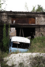 A Blue Van Sits In The Grass Next To A Brick Building In Iļģuciems.