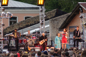 A Group Of People Standing On A Stage In Front Of A Building During Dzelzs Vilks Ielīgo '09.