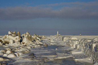 A Winter Scene In Daugavgrīva Featuring Ice-Covered Rocks And A Lighthouse.
