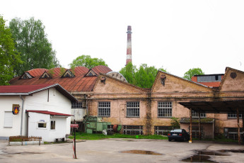 An Old Factory Building In Iļģuciems With A Car Parked In Front Of It.