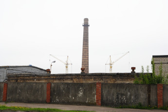 A Tall Chimney Standing Beside A Brick Wall In Iļģuciems.