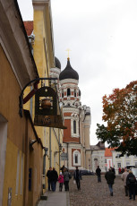 People Walking Down A Cobblestone Street In Tallinn Near A Church.